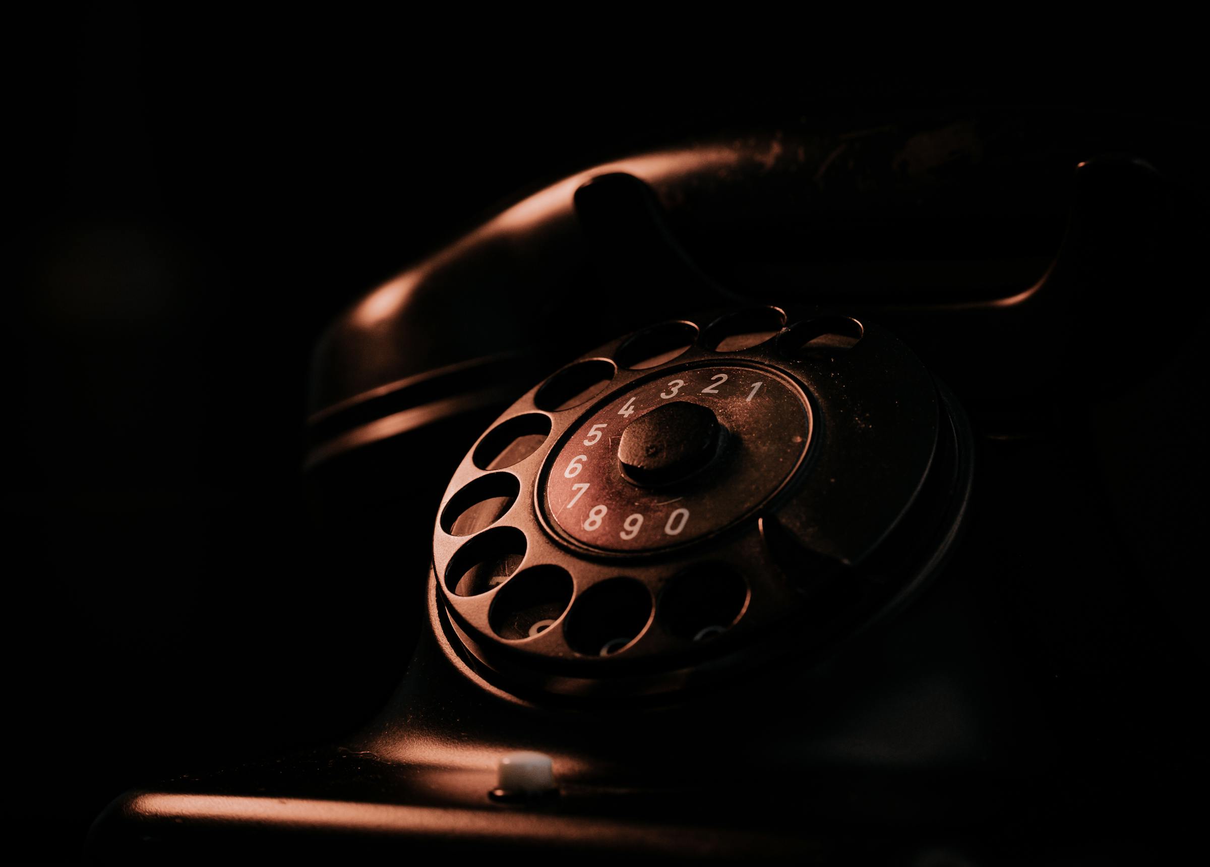 A vintage rotary telephone dramatically lit against darkness — evoking the moment before you pick up and somehow already know who is calling
